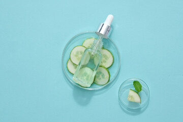 Wall Mural - On a petri dish full of cucumber slices, a glass bottle without label and dropper cap displayed on blue background. Mockup scene for advertising cosmetic with cucumber ingredient