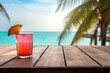 Glass of juice with multicolor wood table, tropical beach, coconut palm tree in background