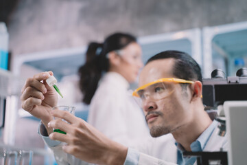 Wall Mural - Researcher man are drop liquid to a beaker in his hand and researcher woman are picking up the remaining substance behind at laboratory.