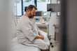 © Halfpoint - Overweight patient in hospital gown waiting for medical examination, test results in hospital, feeling anxious. Patient feeling dizzy, have vertigo and intense pain.