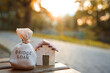 Bridge loan concept - is a short-term loan secured by real estate. Money bag and miniature house in the park in the sunset light. Real estate and finance