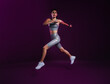 © Artem Varnitsin - Full length of slim woman in silver sports clothes running and jumping over a magenta backdrop