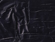Crumpled black plastic surface background. Creased dark plastic texture. Wrinkly wrapper backdrop. Glossy and shiny polyethylene.