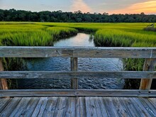 Scenic View Of A Wooden Bridge Over A River And Green Meadow On Jekyll Island, Georgia At Sunset