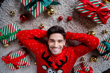 Poster - High angle view portrait of friendly cheerful person toothy smile hands behind head laying carpet floor christmastime giftbox tree bauble toys