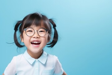 Wall Mural - Close up portrait of a happy asian little girl isolated over blue background.