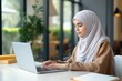© SOLDATOOFF - Young Muslim woman in gray hijab sits at a laptop against the background of modern interior.