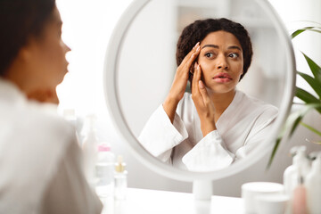 Wall Mural - Sad african american woman looking in mirror at wrinkles around her eyes