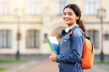 Contented young Indian academic lady with course materials and backpack