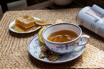 Wall Mural - Morning setup on wooden table at balcony, books to read, cup of natural tea, teapot, organic honey from farm, fresh green tea leaves and organic fruits, in background nice view on small city park 