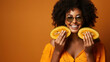 Beauty portrait of dark skinned curly haired young woman holds half of papaya fruit smiles isolated over yellow background. Natural cosmetics concept.