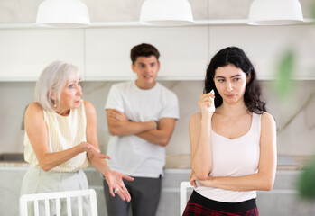 Wall Mural - Upset woman dont speaking after discord with mother and husband standing behind