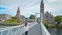 A Tourist With A Camera Explores An Old City In Scotland Walking On A Bridge. A Beautiful Woman Visiting The Old Town Of Inverness, The Largest City And The Cultural Capital Of The Scottish Highlands.
