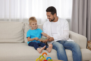 Sticker - Motor skills development. Happy father helping his son to play with geoboard and rubber bands on sofa at home