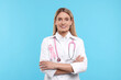 Doctor with pink ribbon and stethoscope on light blue background. Breast cancer awareness