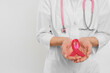 Doctor with stethoscope holding pink ribbon on white background, closeup and space for text. Breast cancer awareness