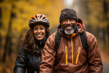Elderly Smiling Couple In Safety Helmets Riding Bicycles Together To Stay Fit And Healthy. African American Seniors Having Fun On A Bike Ride In Autumn Park. Retired People Lead Active Lifestyle.