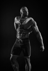 Silhouette of a strong bodybuilder. Confident young fitness athlete with a powerful body and perfect abs. Black and white photography. Dramatic light.