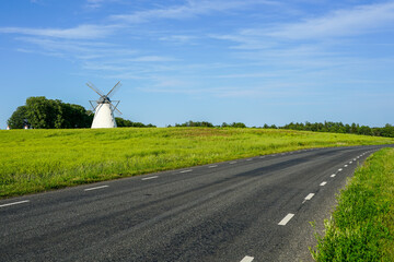 Beautiful summer landscape with blue sky, white windmill, green field and black asphalt road