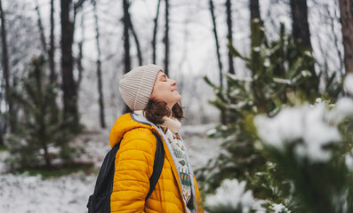 Young adult caucasian woman in a hat and yellow jacket walking n the winter forest breathing fresh air