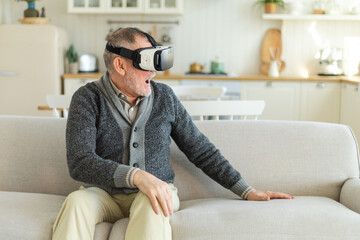 Wall Mural - Excited mature senior man wearing using virtual reality metaverse VR glasses headset at home. Grandfather touching air during VR experience on virtual reality helmet. Simulation hi-tech videogame