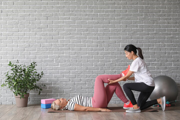 Canvas Print - Mature woman training on mat with therapist in rehabilitation center