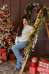 Wall Mural - Woman in jeans and sweater posing in christmas decorated room