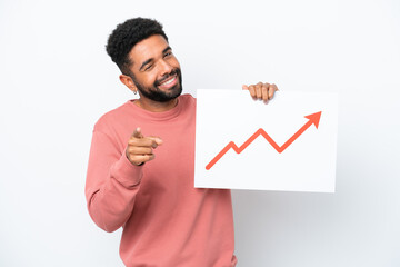 Wall Mural - Young Brazilian man isolated on white background holding a sign with a growing statistics arrow symbol and pointing to the front