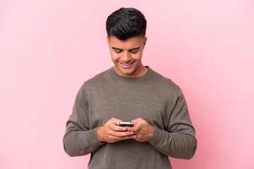 Wall Mural - Young caucasian handsome man isolated on pink background sending a message with the mobile