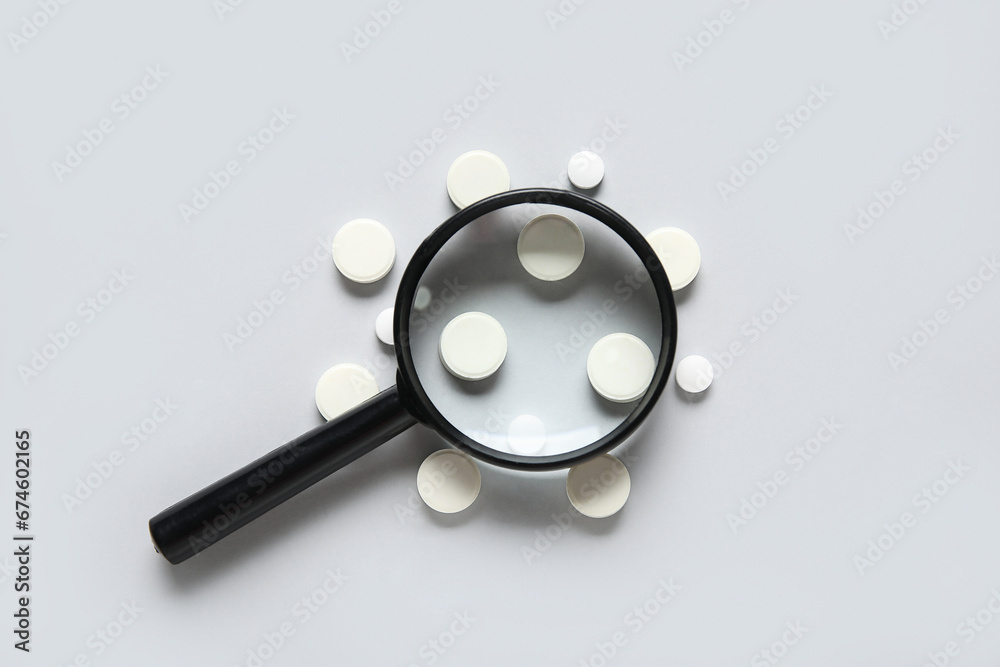 Magnifier with pills on grey background