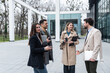 © Srdjan - Group of successful young business people, leaders in marketing and motivation, stand in front of office building and consult before a meeting with employees. HR communication in companies concept