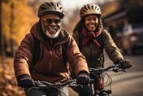 Happy smiling elderly couple in safety helmets riding bicycles together to stay fit and healthy. African American seniors having fun on a bike ride in autumn park. Active lifestyle for retired people.