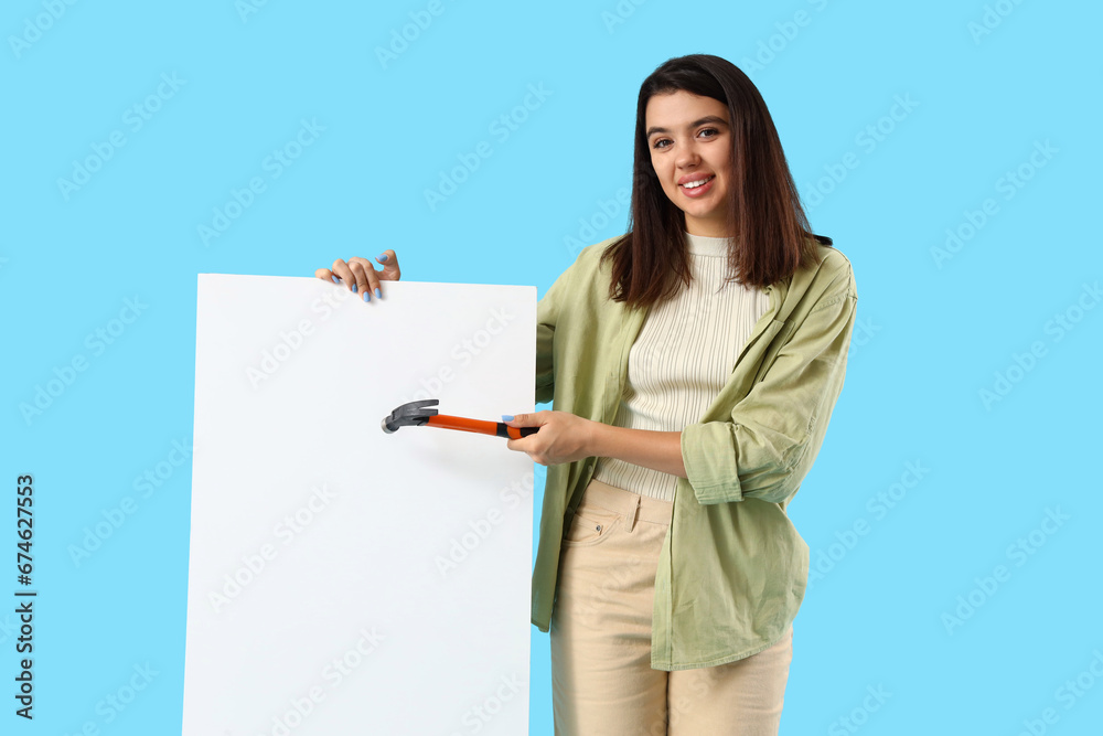 Young woman with hammer and blank poster on blue background