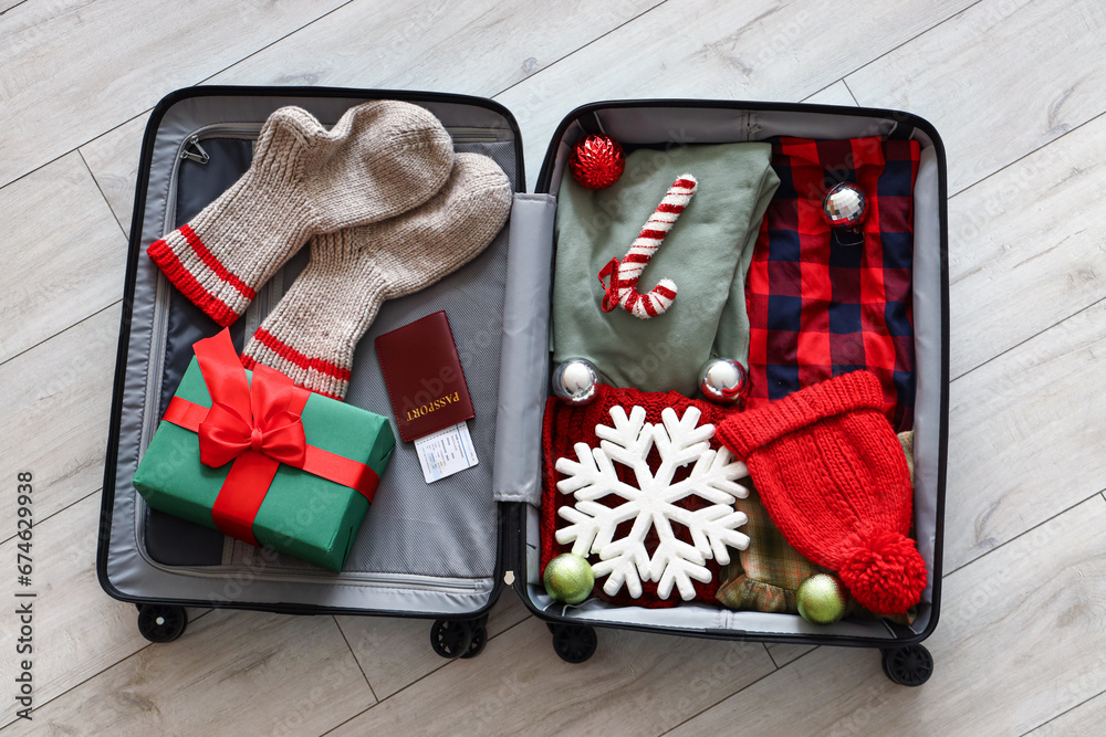 Open suitcase with winter clothes and Christmas gift on floor, top view