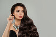 © millaf (Nemchinova) - Stylish fashion model woman brunette with long shiny curly hair, diamond jewelry earring and necklace on gray background, fashion beauty portrait