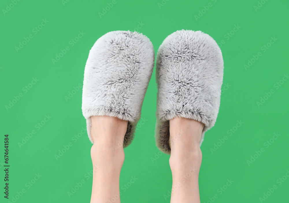 Female legs in soft slippers on green background