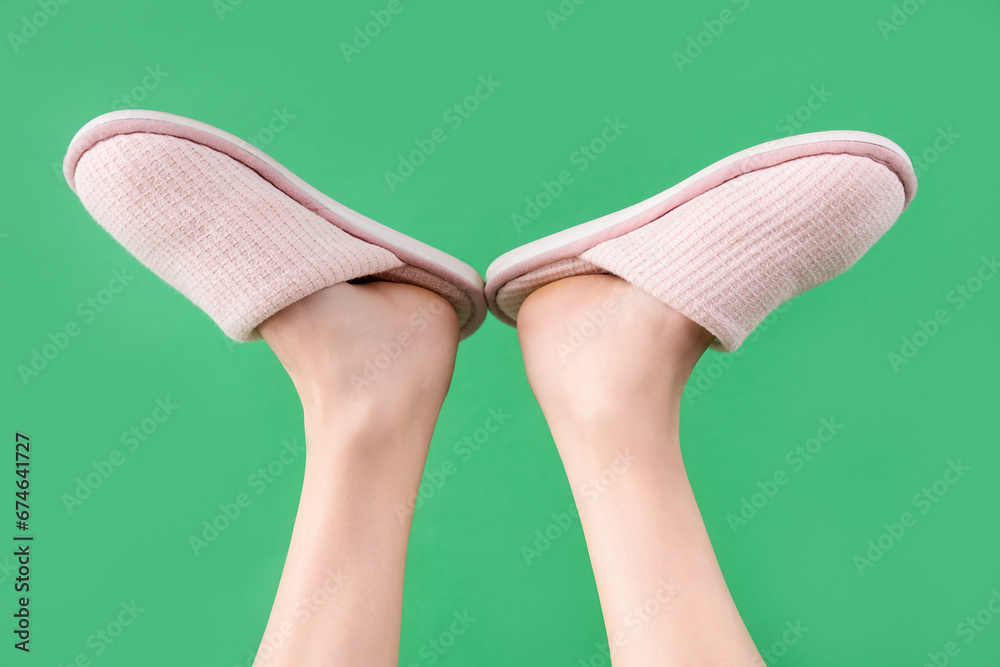 Female legs in soft slippers on green background