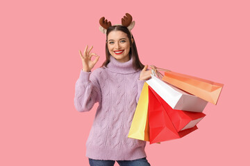 Sticker - Young woman holding shopping bags and showing Ok on pink background