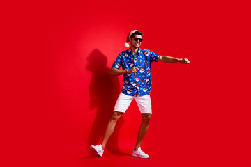 Wall Mural - Full size photo of funky young man dancing have fun wear santa claus print x-mas clothes isolated on red color background