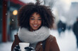 Portrait of a beautiful pretty young stylish dark-skinned woman enjoying a cup of warm beverage coffee during daytime outdoors under the snowflakes at the christmas market during winter holidays