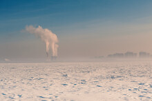 Winter Landscape With Snow Covered Ice, City And Pipes With Thick Steam
