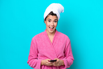 Wall Mural - Young Brazilian woman with a bathrobe isolated on blue background surprised and sending a message