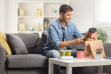 Poster - Happy young man sitting on a sofa and opening takeaway food boxes