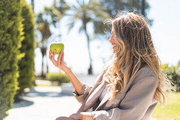 Wall Mural - Pretty blonde Uruguayan woman with an apple at outdoors with happy expression