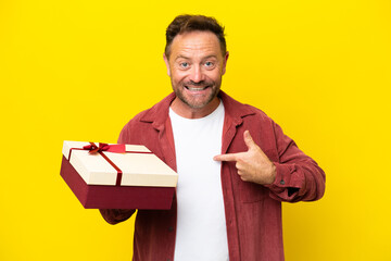 Wall Mural - Middle age caucasian man holding a gift isolated on yellow background with surprise facial expression