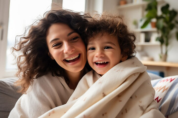 Wall Mural - Happy young Latin mother and little son having fun on cozy couch in living room, overjoyed mum and preschool child tickling, cuddling, enjoying leisure time together