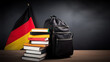 © Maxim Kukurund - The concept of German language courses. School backpack, books and textbooks on the background of the flag of Germany. Humanitarian visa for refugees, emigration for specialists, study or travel. 16:9