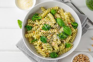 Wall Mural - Vegetarian pasta with pesto sauce, broccoli, parmesan cheese and pine nuts on a white wooden background. Healthy food.