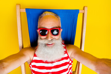 Sticker - Closeup selfie shot of blogging old funny cheerful man in swimming pool wearing swimsuit lying sunbed isolated on yellow color background