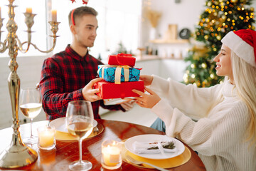 Wall Mural - Beautiful couple in love near the Christmas tree, celebrating the exchange of gifts, spending time together. Holiday concept.